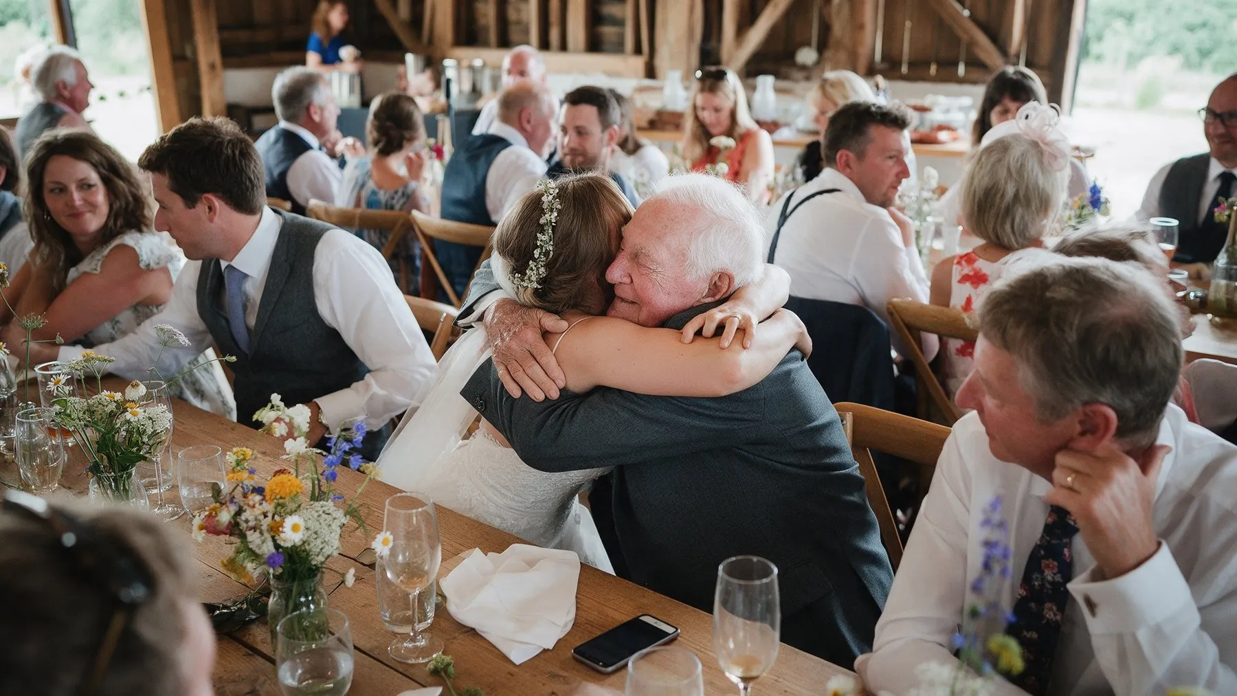Die Braut umarmt ihren Großvater an der Hochzeitstafel